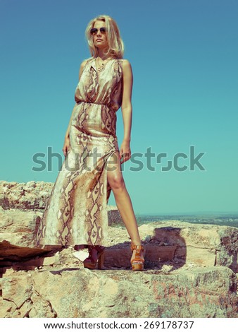 Blonde woman in dress on the rocks. Summer day. Fashion style. Summer wind.