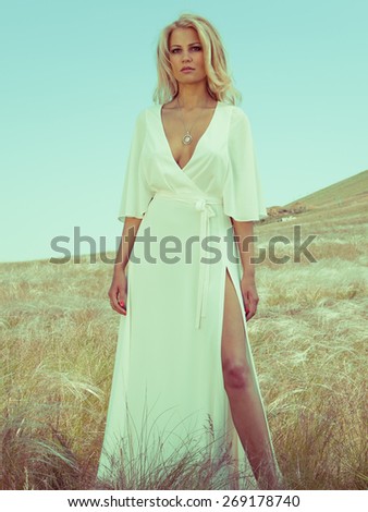 Blonde woman in white dress on the rocks. Summer day. Fashion style. Summer wind.