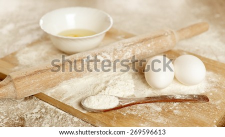 Preparations for homemade baking. Basic ingredients for baking. Kitchen utensil with eggs rolling-pin wood spoon meal. Meal on table with cutting board. Flour. baking