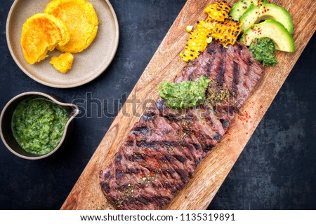 Barbecue dry aged wagyu flank steak with arepas corn, and chimichurri sauce as top view on a cutting board