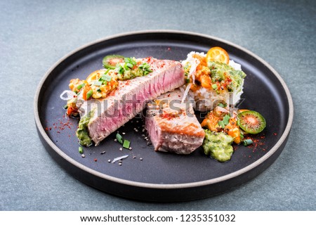 Traditional exotically tuna fish fillet with mango salsa and rice as closeup on a modern design black plate