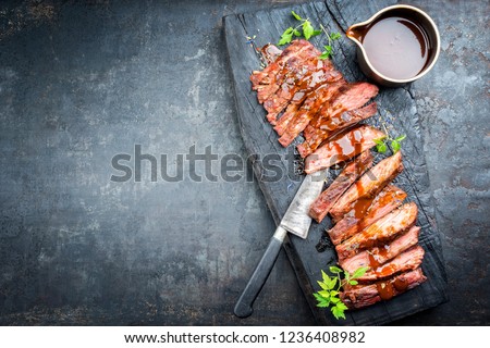 Traditional American barbecue dry aged flank steak sliced with hot sauce and chili as top view on an old carbonized board with copy space left