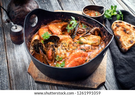 Traditional Catalan fish stew romesco de peix with prawns, mussels and fish as closeup in a modern design cast-iron roasting dish