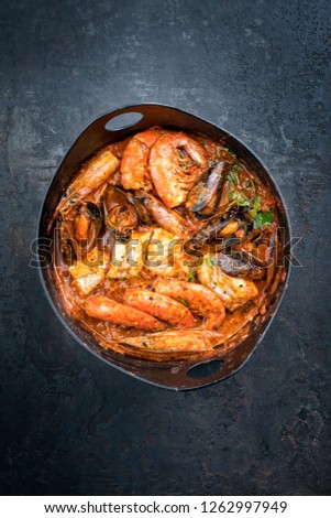 Traditional Catalan fish stew romesco de peix with prawns, mussels and fish as top view in a modern design cast-iron roasting dish with copy space