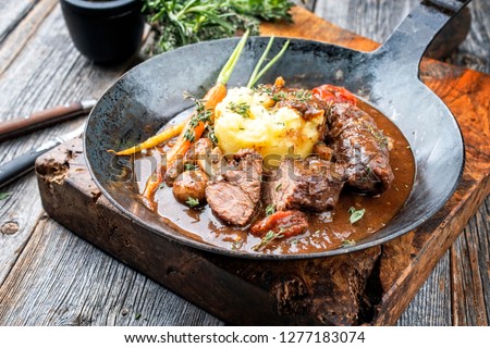 Traditional German braised pork cheeks in brown sauce with mushroom and mashed potatoes as closeup wrought-iron pan