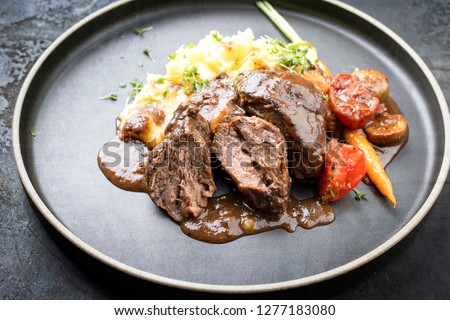 Traditional German braised pork cheeks in brown sauce with mushroom and mashed potatoes as closeup on a modern design plate