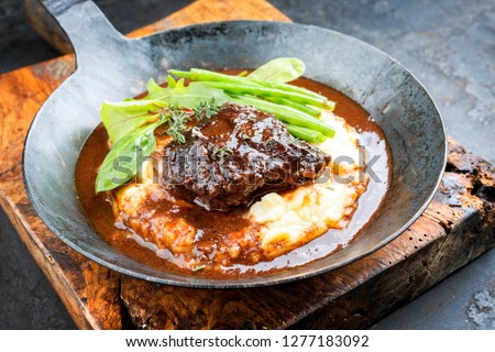 Traditional German braised veal cheeks in brown sauce with mashed potatoes and beans as closeup in a wrought-iron pan