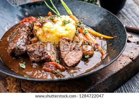 Traditional German braised pork cheeks in brown sauce with mushroom and mashed potatoes as closeup wrought-iron pan