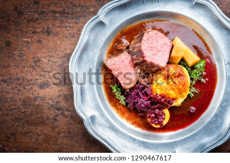 Traditional saddle of venison with fried mashed potatoes and red cabbage in game red wine sauce as top view on a pewter plate with copy space left
