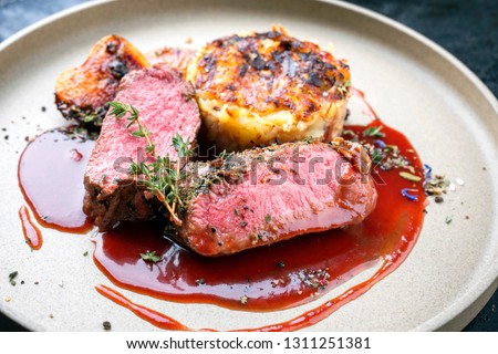 Traditional saddle of venison with Swiss rösti, quince and orange slices in game red wine sauce as closeup on a modern design plate