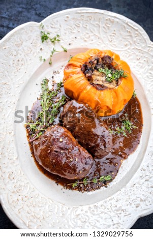 Traditional German braised pork cheeks in brown red wine sauce with mushroom and pumpkin as closeup on a shabby chic design white plate