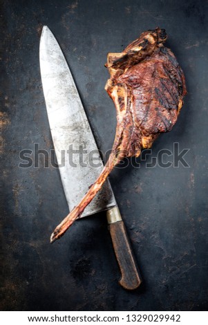 Traditional barbecue dry aged wagyu tomahawk steak as top view on an old rustic metal sheet with a large knife