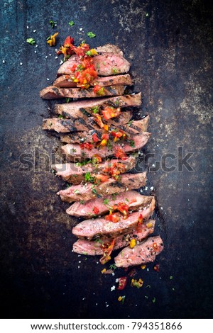 Traditional American barbecue dry aged flank steak sliced with a relish as close-up on a board