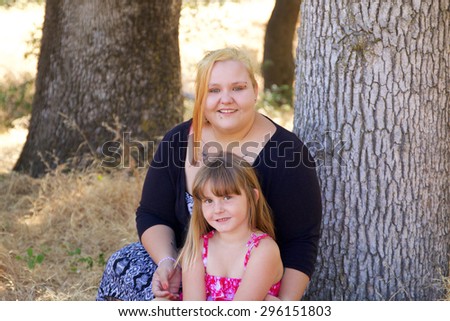 Tattooed mother with her you daughter sitting by a tree in a park