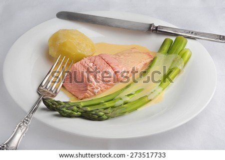 Green asparagus and poached salmon with sauce maltaise (hollandaise variation) with a potato on a white plate with old style silverware.