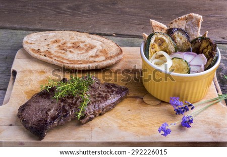 Provencal style horse meat entrecote steak with ratatouille and flat bread served on a wooden board decorated with lavender and fresh thyme.