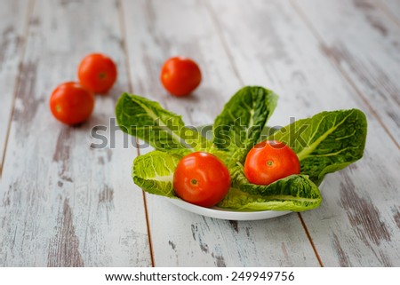 Red tomatoes with salad leaves on white dish