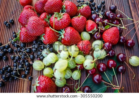 Mix of fresh and juicy berries in the summer garden on wooden texture background