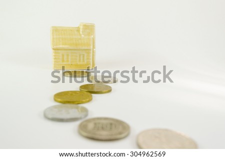 Miniature house with arranged coins leading to house, isolated on white background