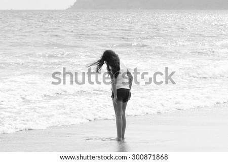 Caucasian Girl Standing On The Coronado Island Ocean Coastline With Foamy White Tidal Waves Rising To Shore In California Against Hilly Background In The Distance In Black & White