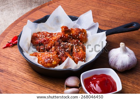 Chicken wings on cast iron pan with spices and sauce on wooden background