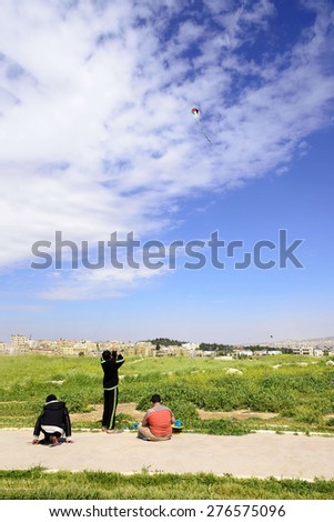 Amman, Jordan - April 03, 2015: View of three jordanian boys playing with kite in Amman Citadel. A kite is an aircraft consisting of one or more wings tethered to an anchor system used for recreation