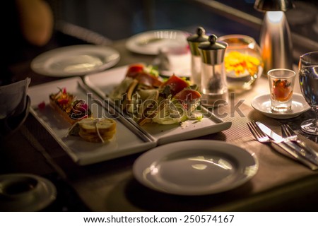 Plates and Dishes on the table in luxury restaurant. Sushi roll with salad. Romantic dinner with ambient light from candle.