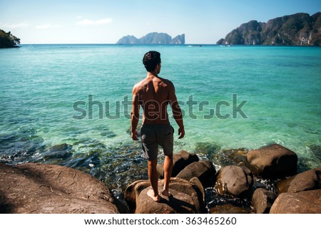 Man turned back to the camera looking at the sea, relaxed, concept of freedom. Gym handsome brunette hair man with nude torso on the beach in Phi Phi island, Thailand