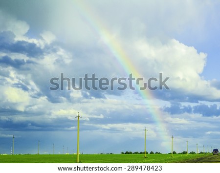 bright rainbow in the stormy sky over the green meadow