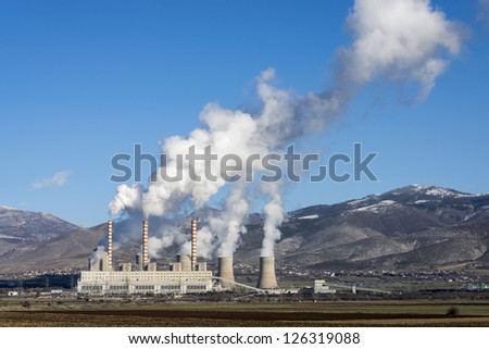 Fossil fuel power plant in full operation, emitting smoke.
