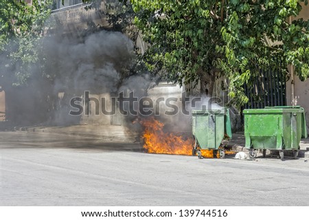 Waste container on wheels, set on fire, emitting smoke