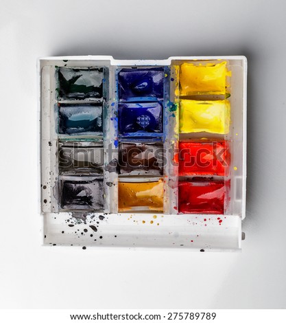 An open box of paints. Watercolor paints on a white background. Bright colors slightly moistened with water.
