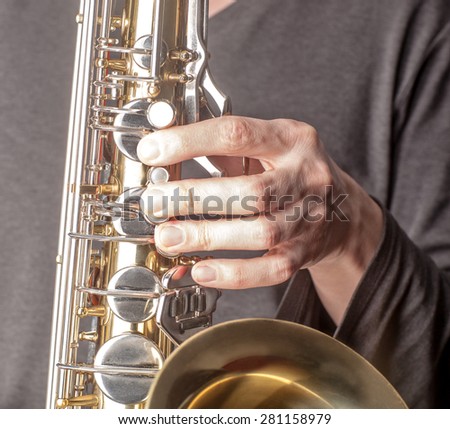 Fragment of top part Tenor Saxophone. Left hand is playing. Tenor sax close up. Close up of keys tenor saxophone. Wonderful instrument.