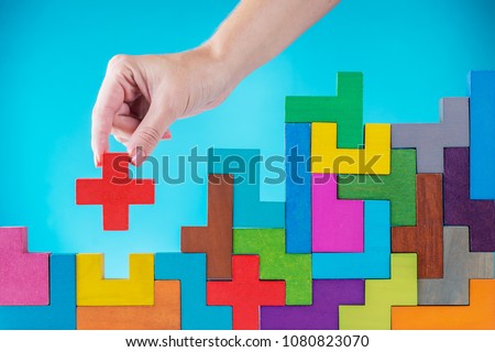 Concept of decision making process, logical thinking. Logical tasks. Conundrum, find the missing piece of the proposed. Hand holding puzzle element. Background with colorful shapes wooden blocks