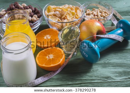 The concept of a healthy lifestyle. Cornflakes, orange juice, yogurt, nuts, honey, tangerines, apple, dumbbell  and measuring tape on rustic wooden table.\
Cereals and fruit - diet and breakfast