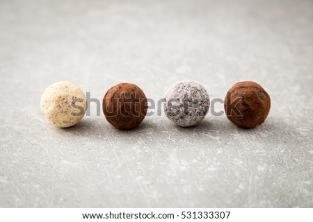 Assorted chocolate truffles with cocoa powder, coconut and chopped hazelnuts on a dessert plate.