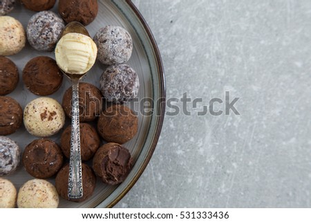Assorted chocolate truffles with cocoa powder, coconut and chopped hazelnuts on a dessert plate.