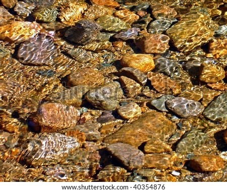 Bangles of light on pebbles in stream.
