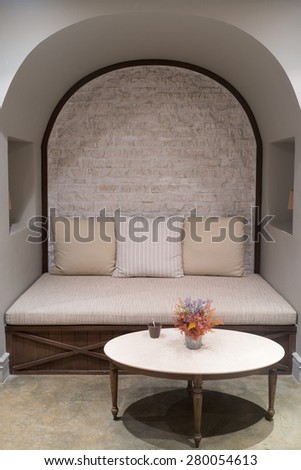 British style living corner with sofa and round table against brick wall.