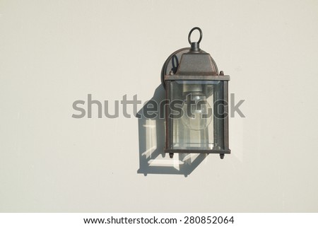 Old rusty outdoor lamp attached on the white wall with its shadow.