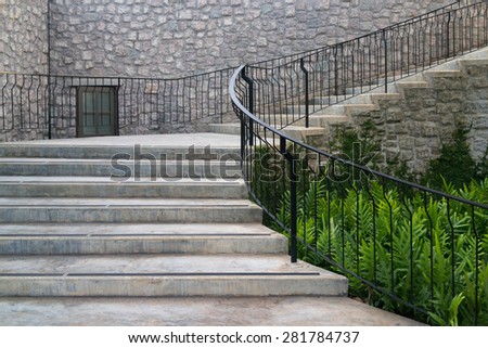 Castle style concrete curve stairways with green ferns and stone veneer wall.