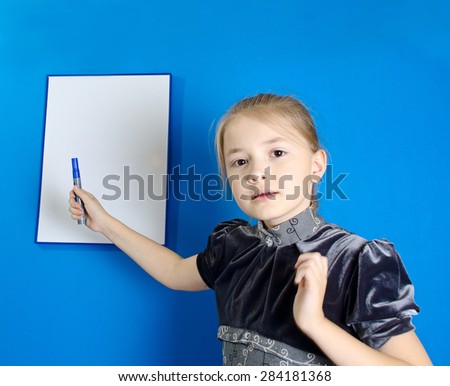 The girl of 9 years in a gray dress shows a marker on a white plastic board where it is possible to place the text.