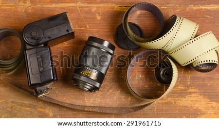 old, negative film for the camera, the cartridge for a film, the lens and flashlight lie on an old wooden table