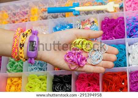 A hand with a bracelet and a set of loom bands to weave