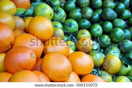 heaps of yellow and green oranges laid side by side in a produce market