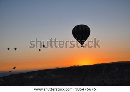 Hot air balloons floating in the air as the sunrise casts a long orange streak lining the far horizon