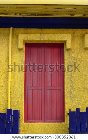 Brick-red wooden door, bright yellow wall and blue-purple fence.