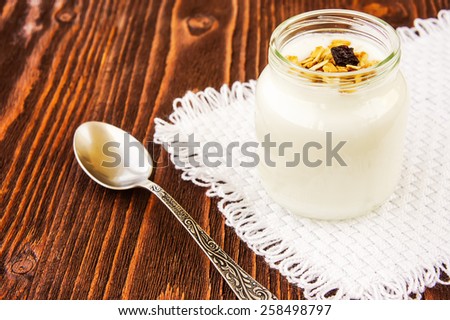 A jar of yogurt with honey glazed oatmeal, nut and coconut chips granola on wooden background
