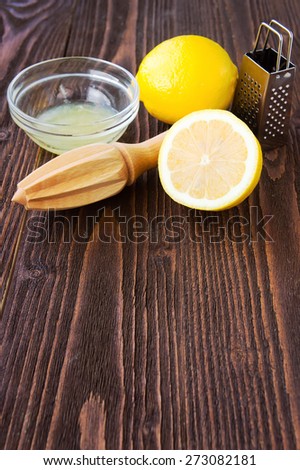 Lemons, lemon juice, wooden citrus squeezer and metal grater on dark wooden board