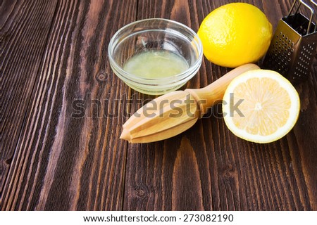 Lemons, lemon juice, wooden citrus squeezer and metal grater on dark wooden board